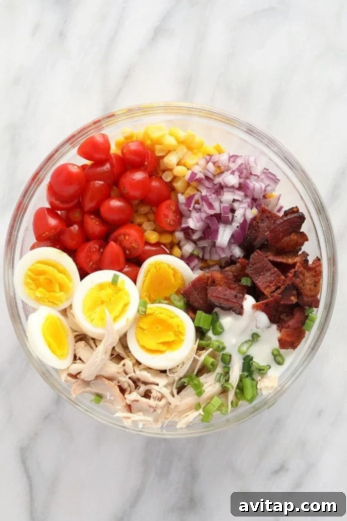 Individual ingredients for Rotisserie Chicken Cobb Salad laid out in a bowl, ready for mixing, including chicken, eggs, bacon, tomatoes, onion, and corn.