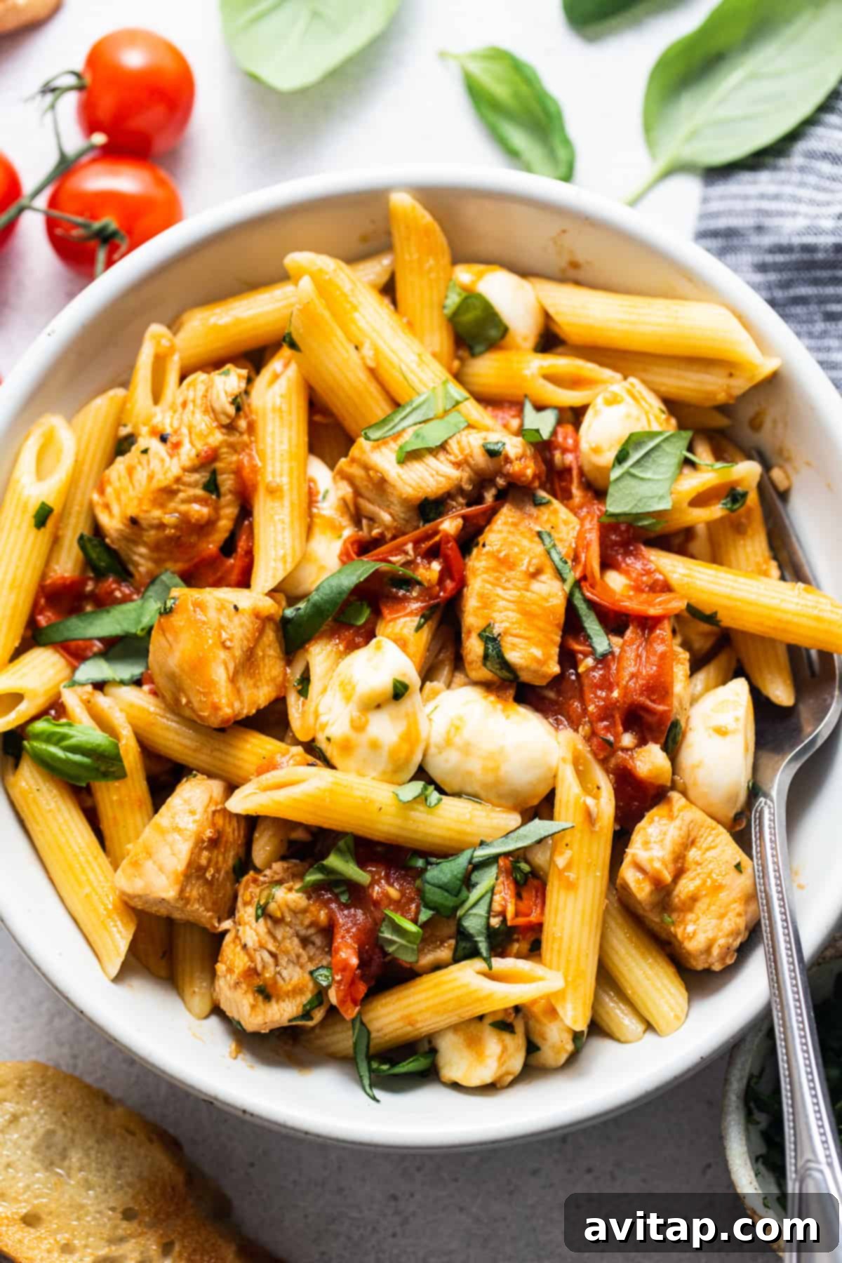 Caprese chicken pasta in a bowl with a fork, garnished with fresh basil.