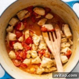 Cooking chicken and cherry tomatoes in a large pot, tomatoes are softening and releasing juices.