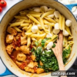 Caprese chicken pasta being tossed in a large pot with mozzarella balls and sauce.