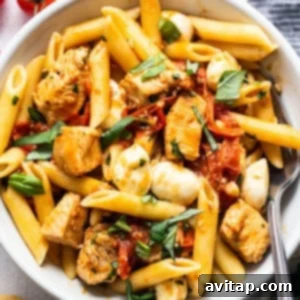 Caprese chicken pasta in a bowl with a fork, ready to serve.