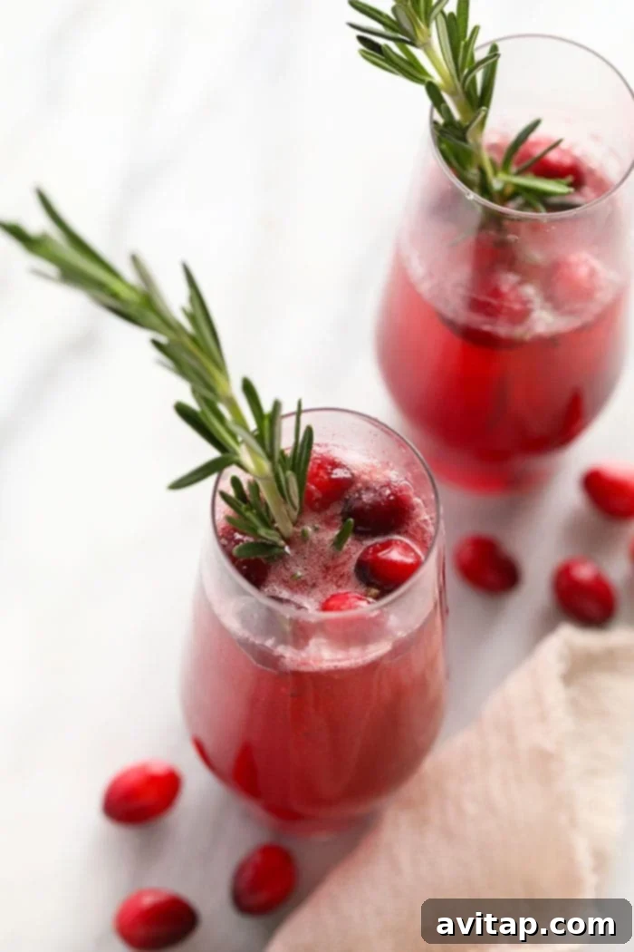 Two glasses of Cranberry Mojitos, garnished with fresh cranberries and rosemary sprigs.