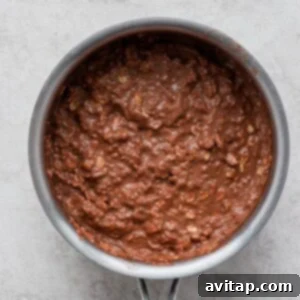 Decadent Chocolate Protein Oats 4 Creamy chocolate protein oatmeal simmering in a pan on a white stovetop.