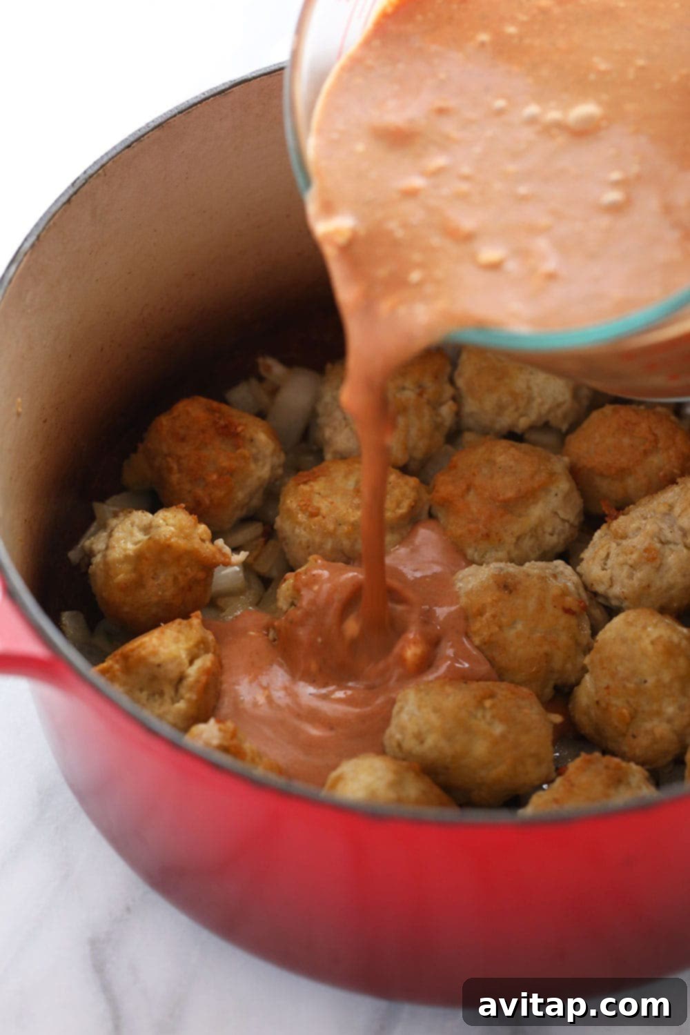 Hello, tikka masala meatballs! Enjoy a bowl of these tikka masala meatballs over a bed of rice, quinoa, or roasted veggies! You can make it for dinner or for a great meal prep dinner for the week! Pouring tikka masala sauce over the meatballs