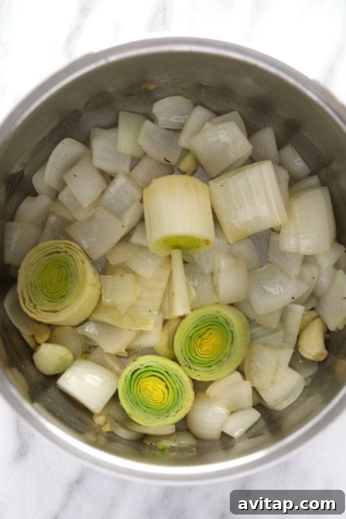 Onions, leeks, and garlic cloves being sautéed in the Instant Pot to build a flavorful base for pot roast