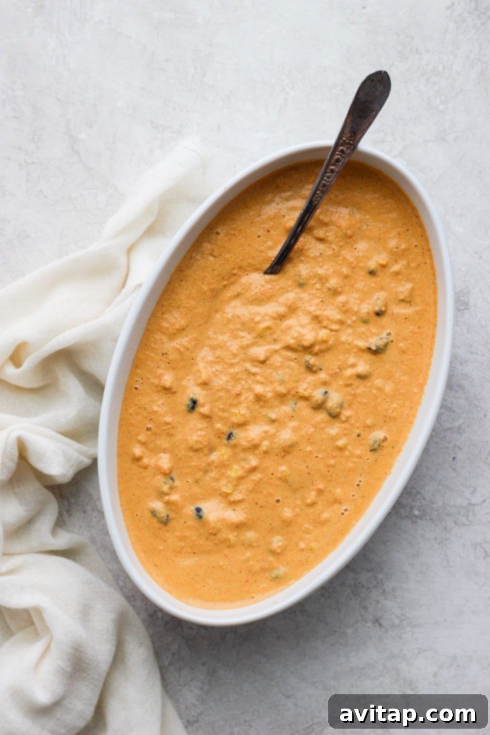 vegan street corn queso dip in a serving bowl with a spoon, showing creamy texture and colorful ingredients