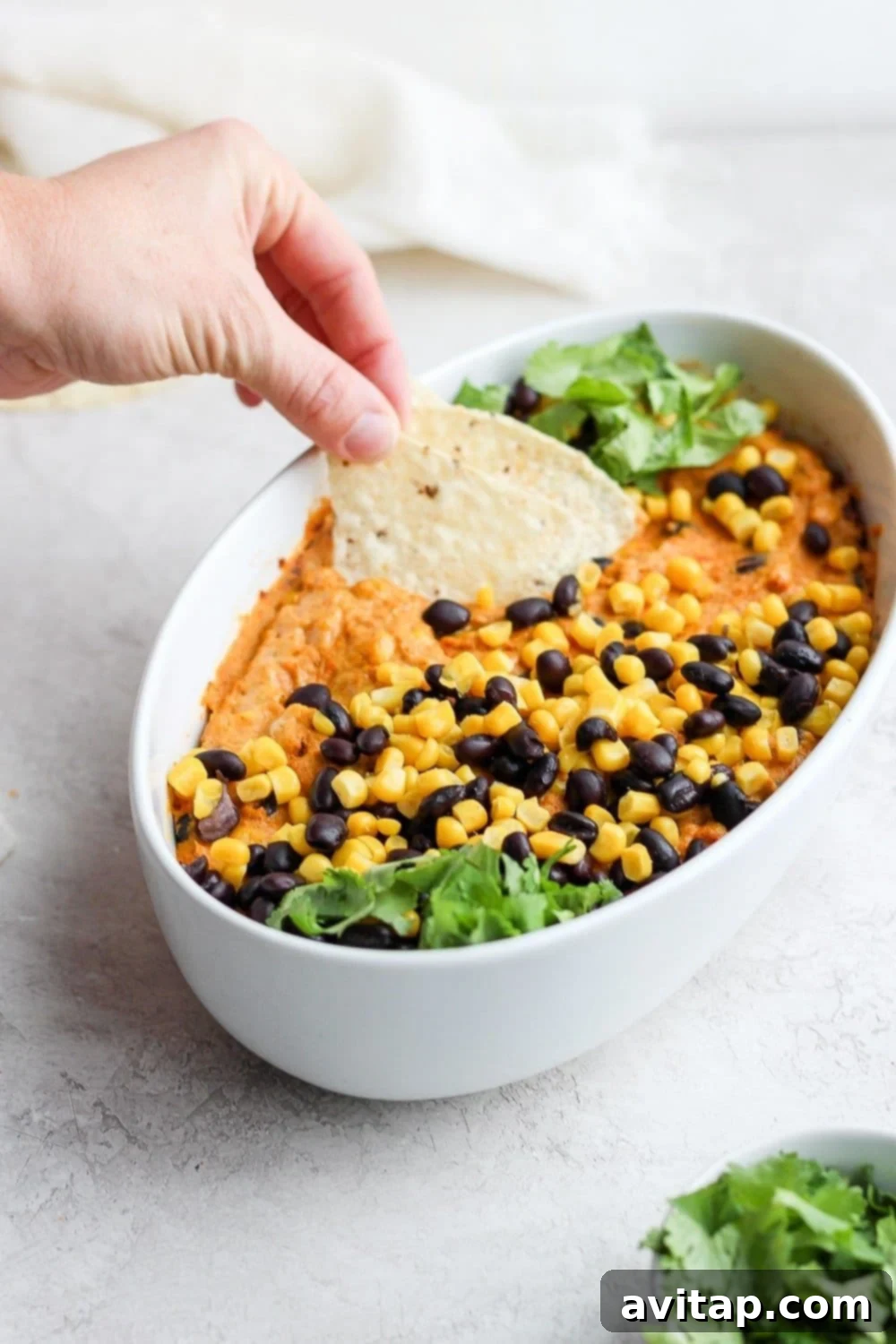 close-up of vegan street corn queso dip with a tortilla chip being dipped into its creamy texture