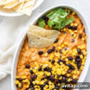 Street corn and queso dip in a white bowl with black beans and cilantro garnish.