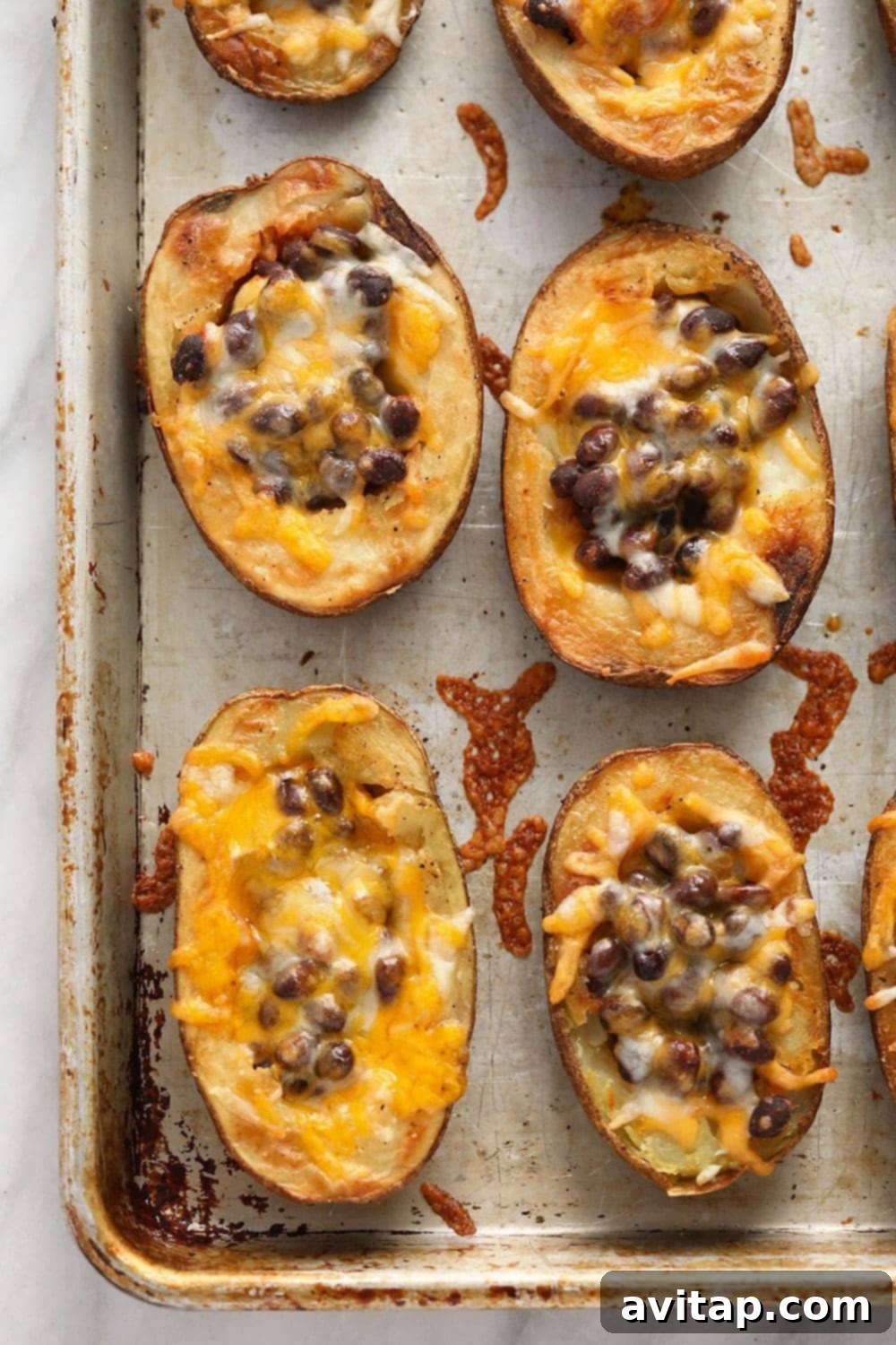 Several crispy, golden-brown potato skin halves are arranged on a baking sheet, ready for their delicious Mexican-inspired toppings.
