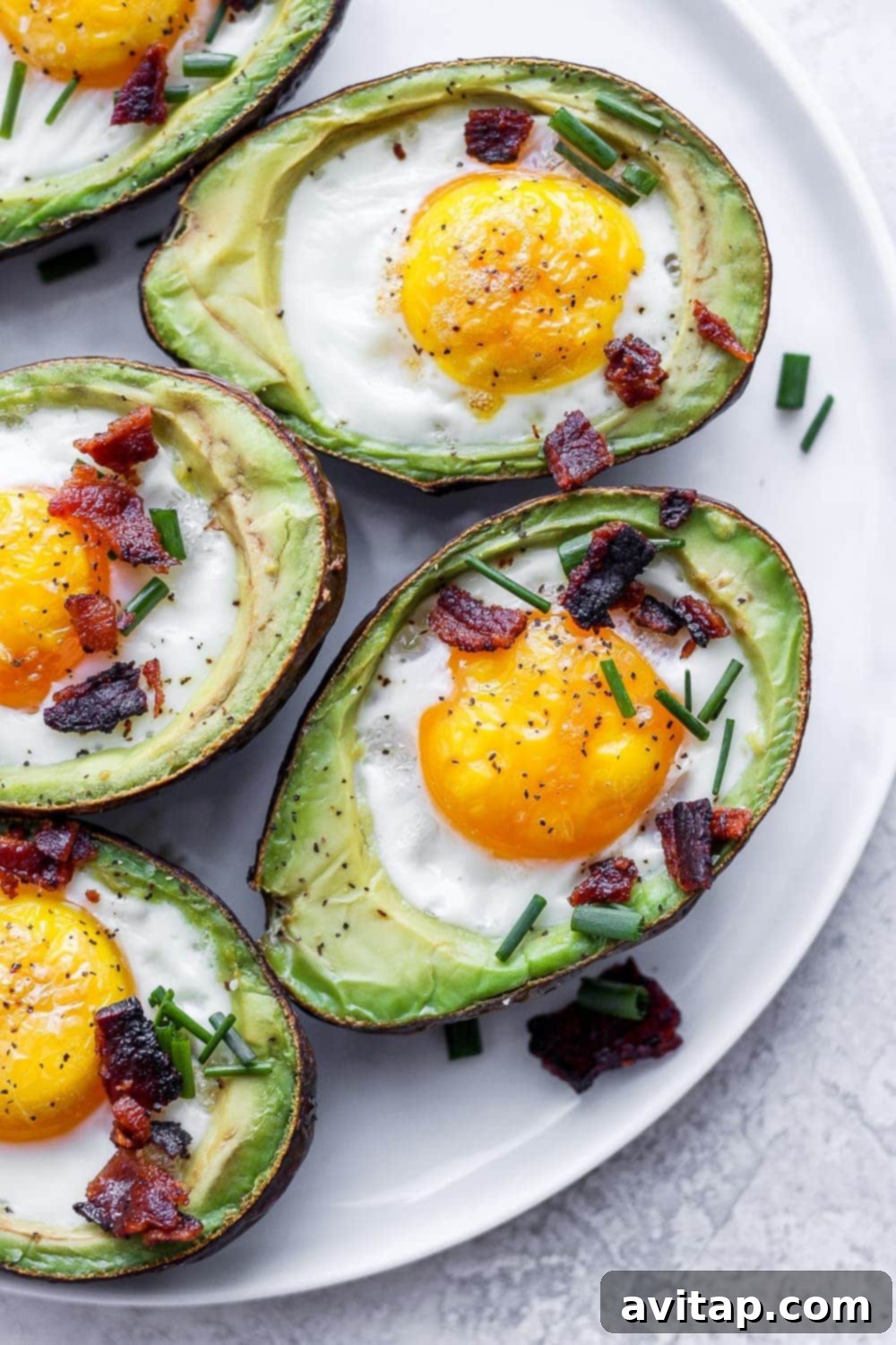 Delicious baked avocado egg topped with crispy bacon and fresh chives, served on a plate for a healthy breakfast.