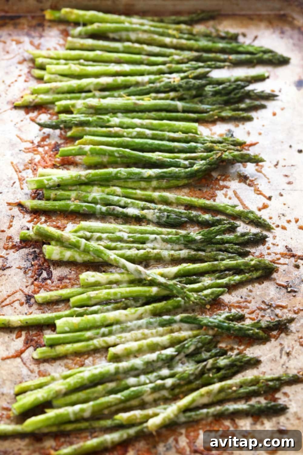 Asparagus spears evenly spread on a baking sheet, ready for oven roasting.