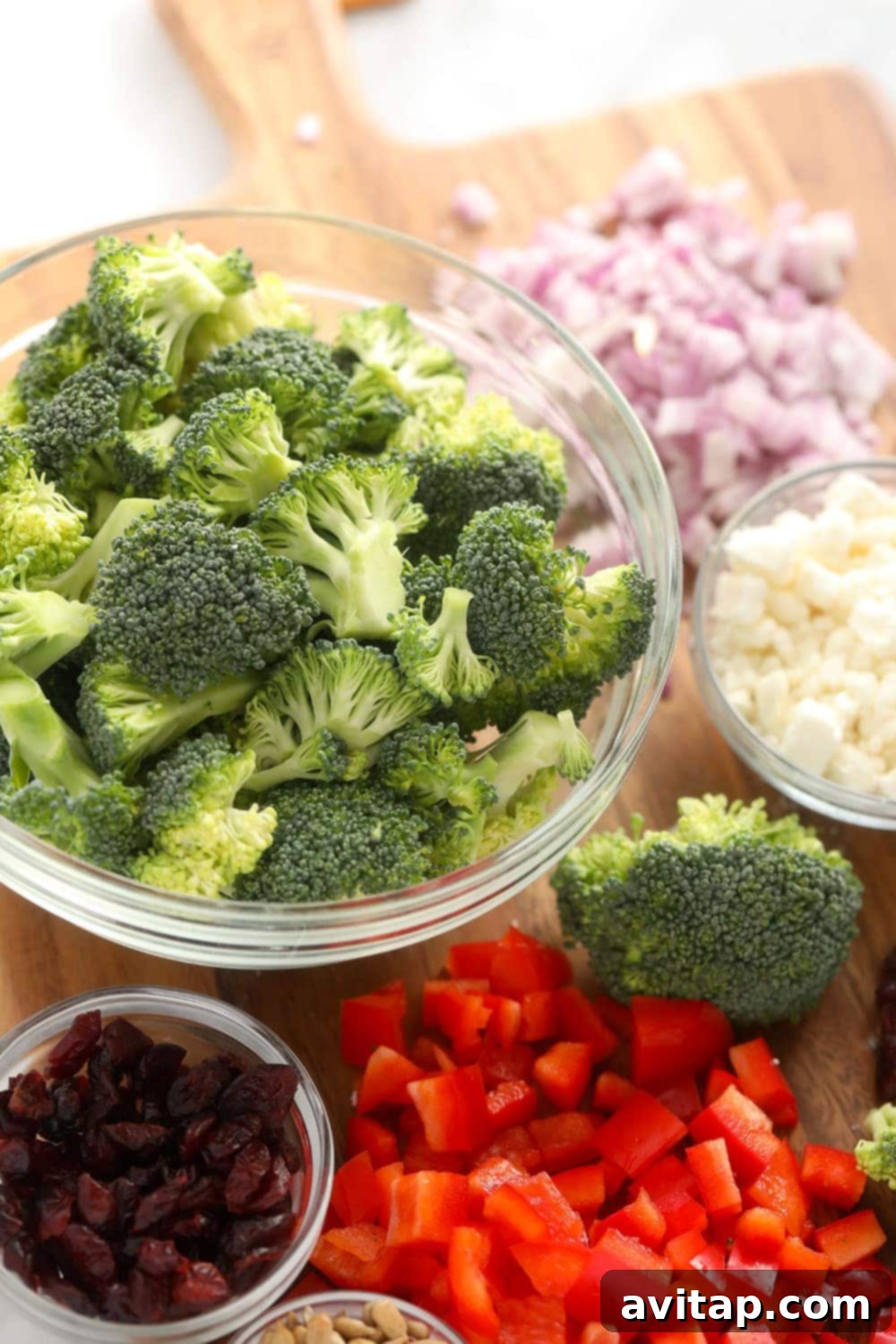 Individual ingredients for broccoli salad, including chopped broccoli, red onion, and red pepper, laid out and ready for preparation