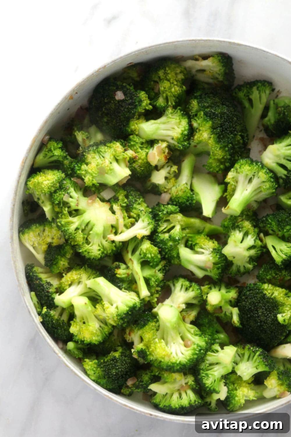 Sautéed broccoli and finely diced red onion being cooked in a large skillet