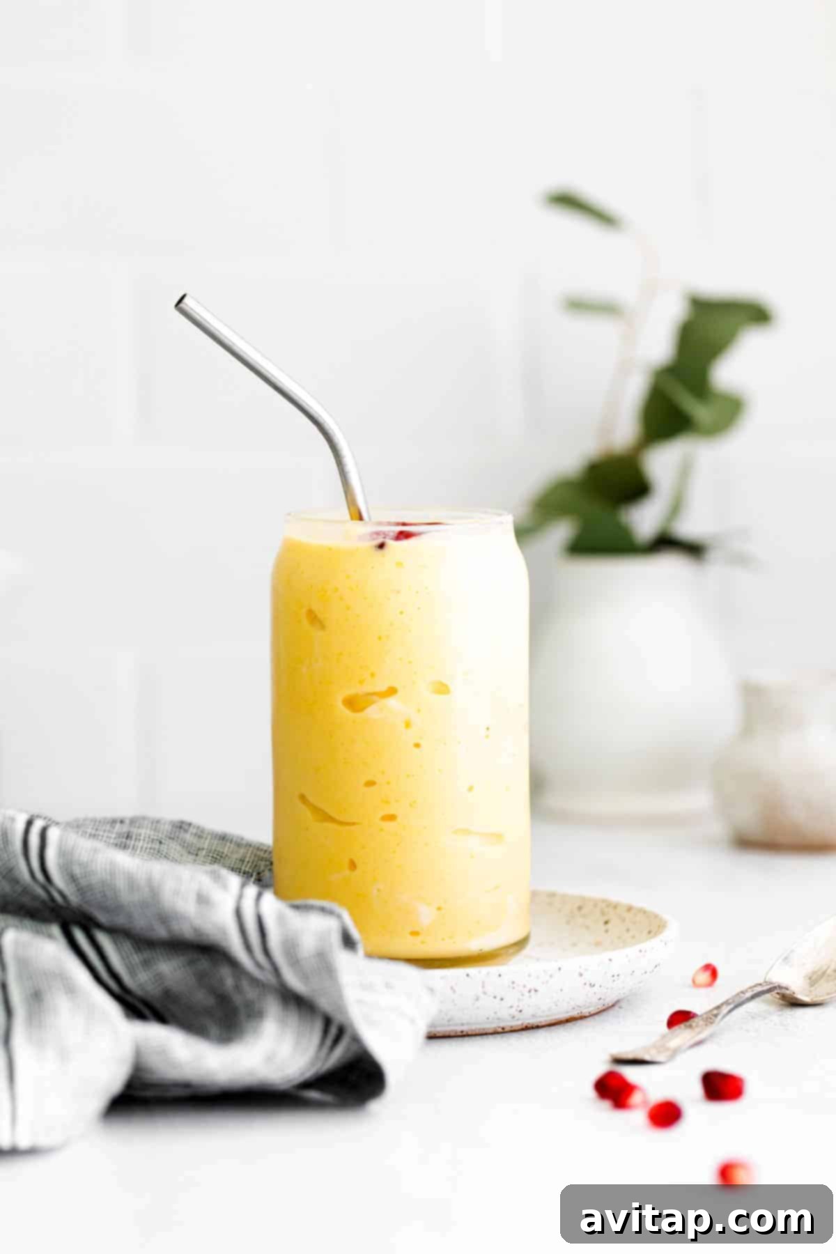 A delicious mango smoothie in a glass, topped with fresh fruit and granola, ready to be enjoyed.