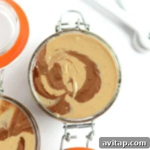 Three jars of homemade nut butter, including chocolate vanilla swirl cashew butter, with a spoon.