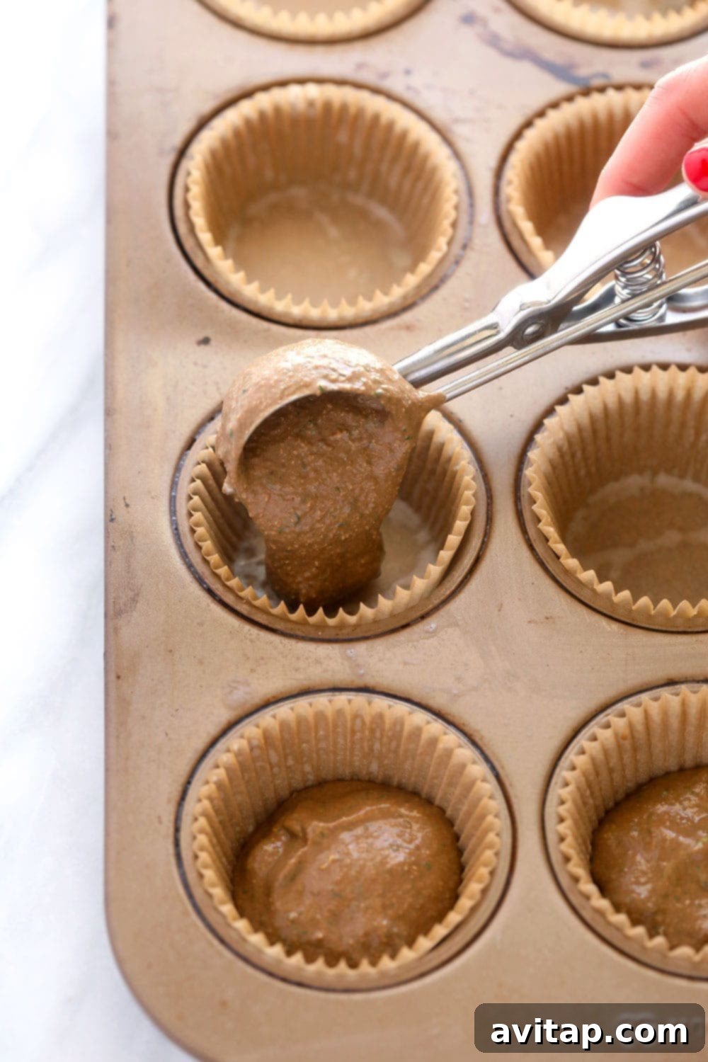 Filling muffin cups with nutrient-rich batter Muffin cups being filled with healthy spinach chocolate chip muffin batter using a cookie scoop.