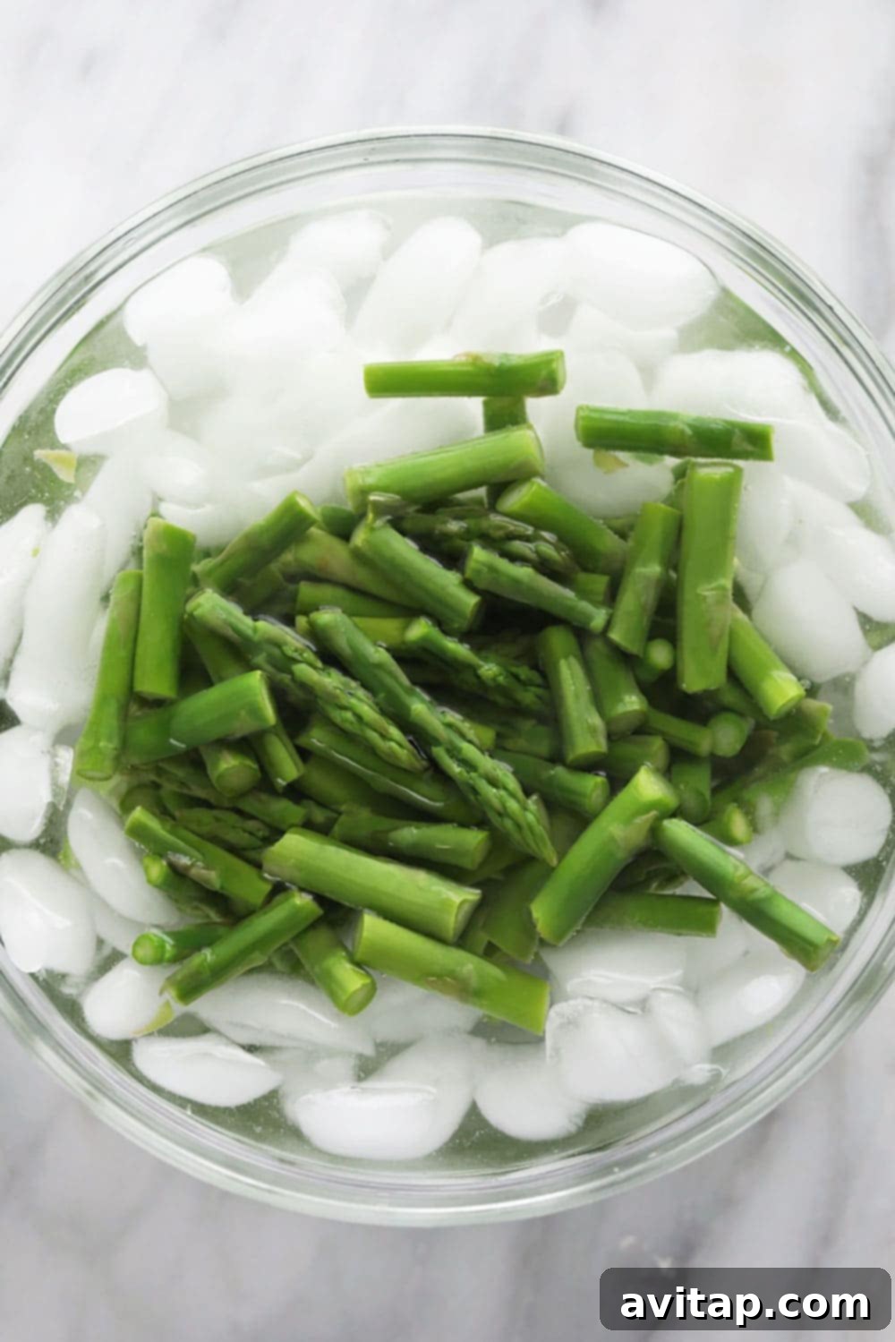 A hand holding tongs, blanching fresh asparagus spears in boiling water.