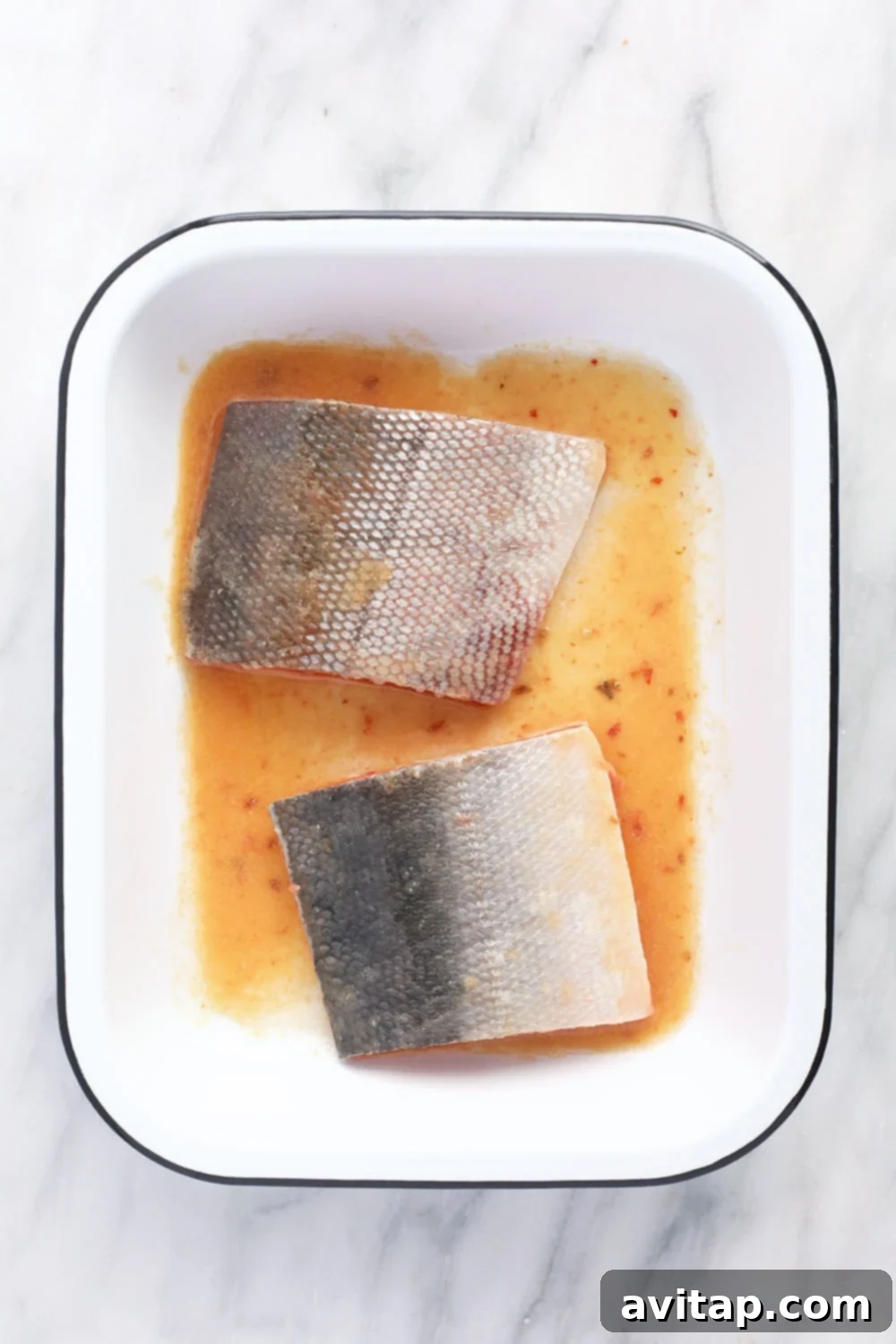 Close-up of fresh salmon fillets soaking in a rich, aromatic miso-ginger marinade in a pan, ready for the oven.