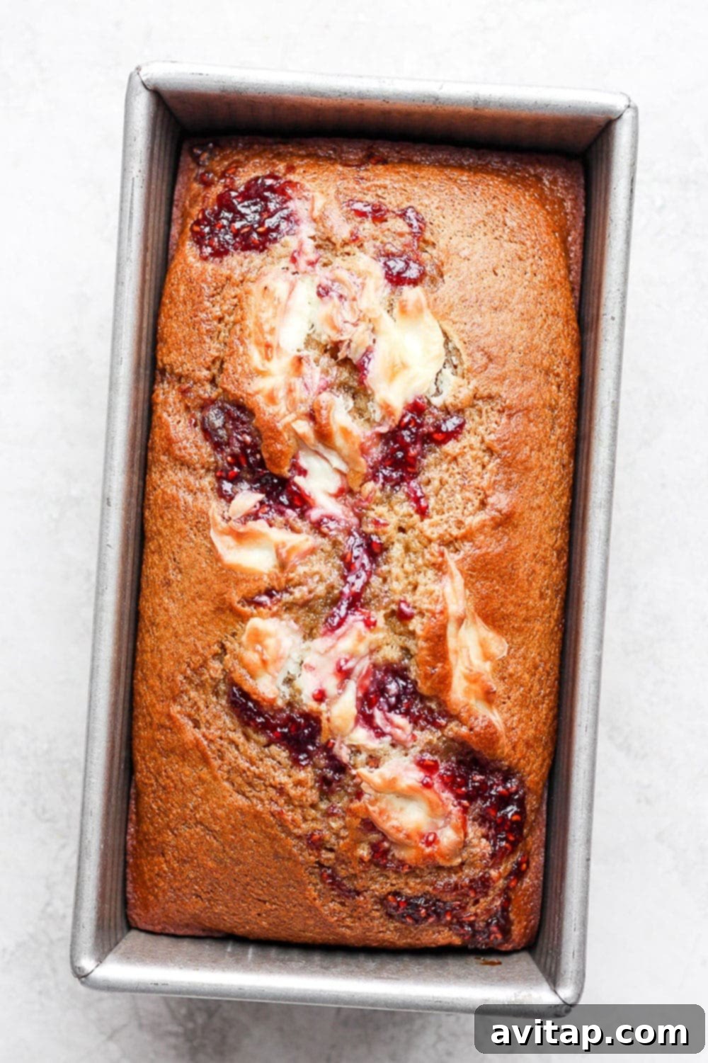 Baked lemon bread with a prominent raspberry and cream cheese swirl cooling in a loaf pan.
