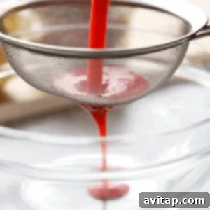 Boozy Strawberry Lemonade 4 Blended strawberries being poured into a sieve over a glass bowl to create a smooth puree.