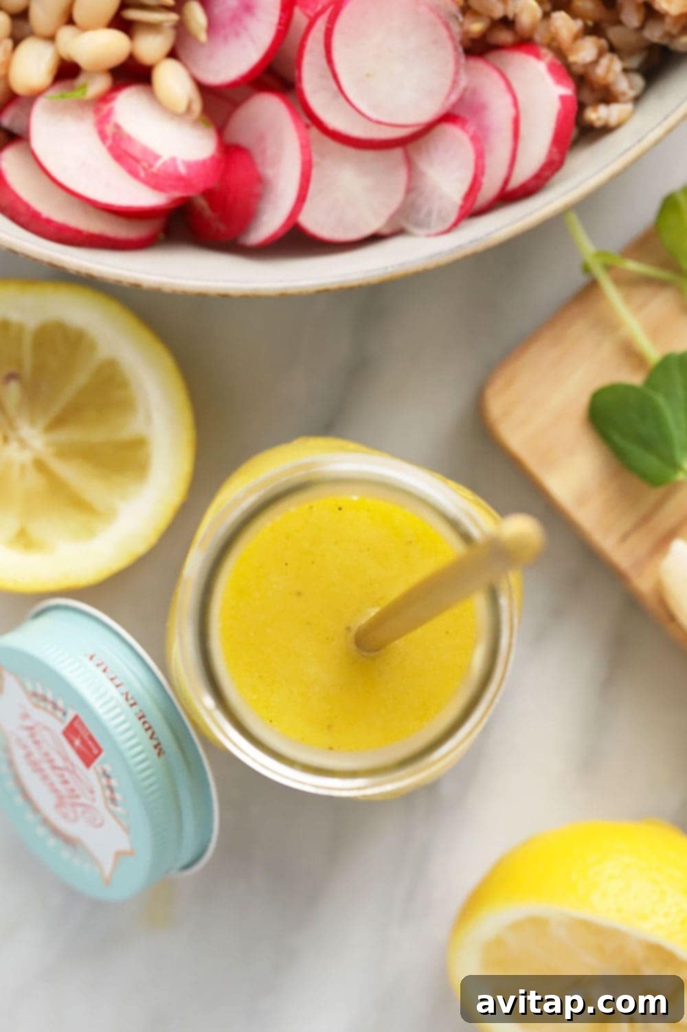 Homemade lemon vinaigrette dressing in a jar with a pouring spout, positioned next to a fresh salad, ready for serving.