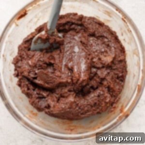 A glass bowl filled with thick, chocolate cookie dough and a gray spatula resting inside, showing the ideal consistency.
