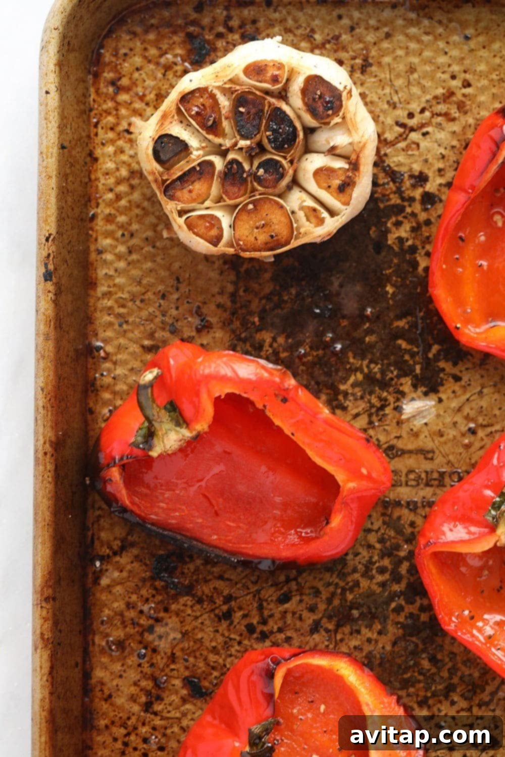 Fresh red bell peppers, halved and seeded, alongside whole peeled garlic cloves, arranged on an oiled baking sheet, ready for roasting.