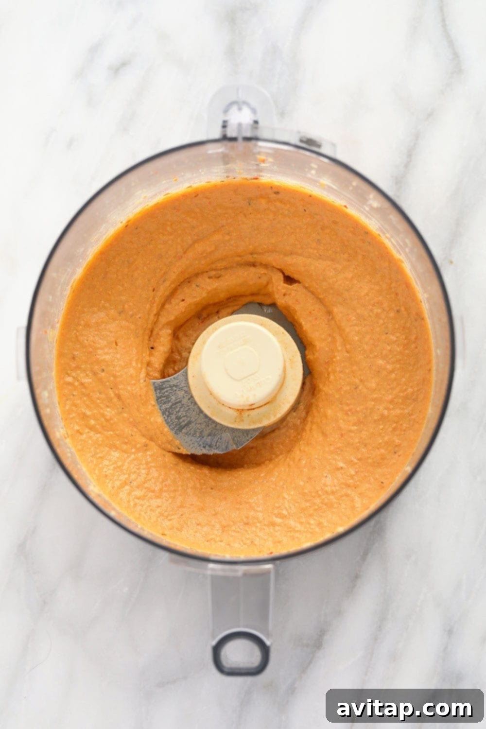 Smooth and perfectly blended roasted red pepper hummus inside a food processor bowl, showcasing its creamy texture.