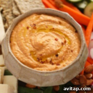 A bowl of creamy roasted red pepper hummus, garnished with a drizzle of olive oil and fresh parsley, ready to be served.