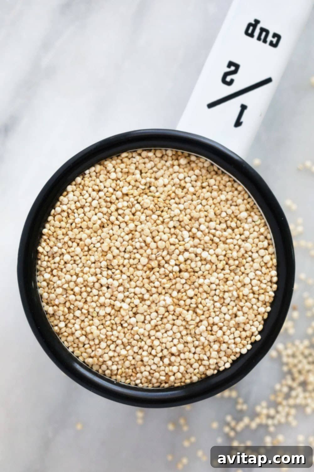 Did you know that quinoa isn't a grain and it's actually a seed? We're sharing quinoa nutrition facts and ways to make quinoa taste good! Uncooked quinoa measured in a cup, highlighting its small seed-like appearance.