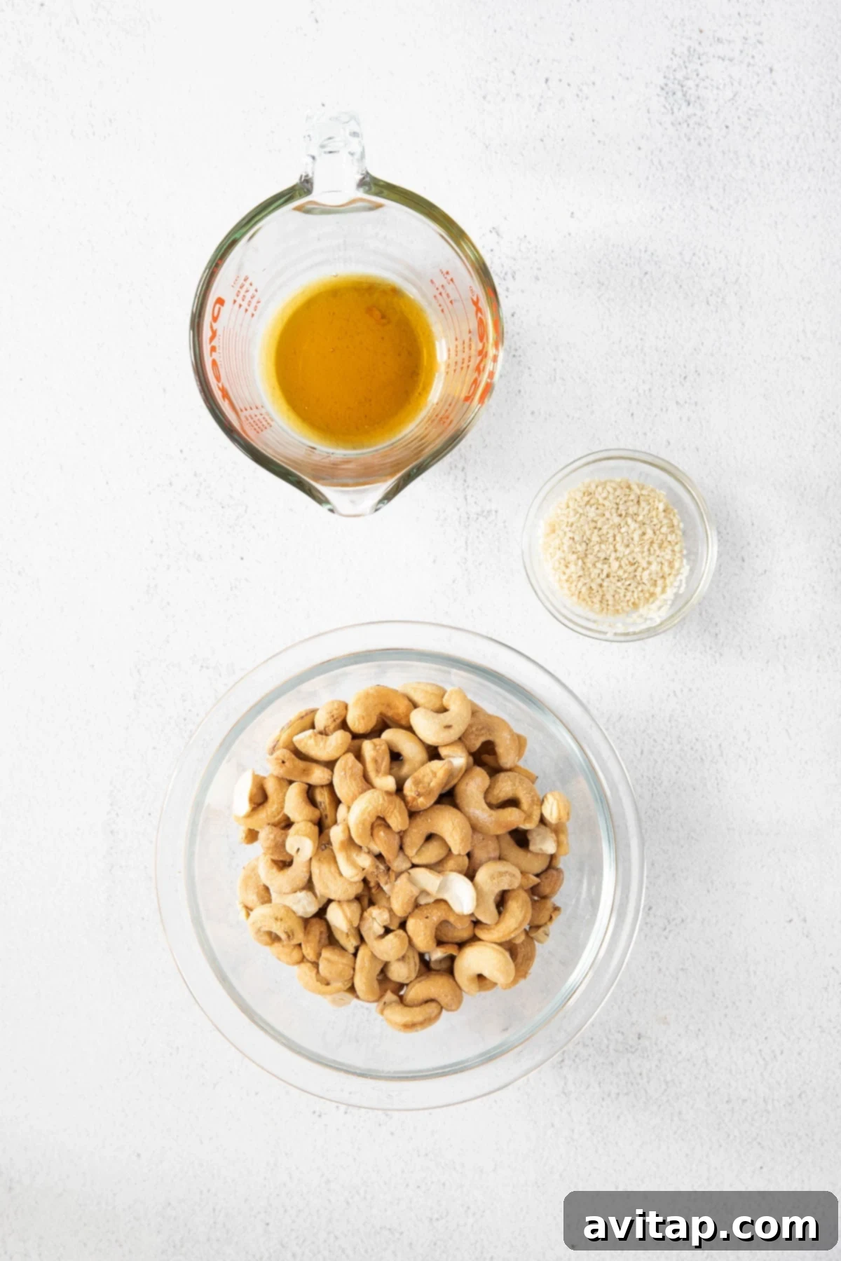 Ingredients for maple sesame roasted cashews: raw cashews, maple syrup, and sesame seeds laid out on a surface.
