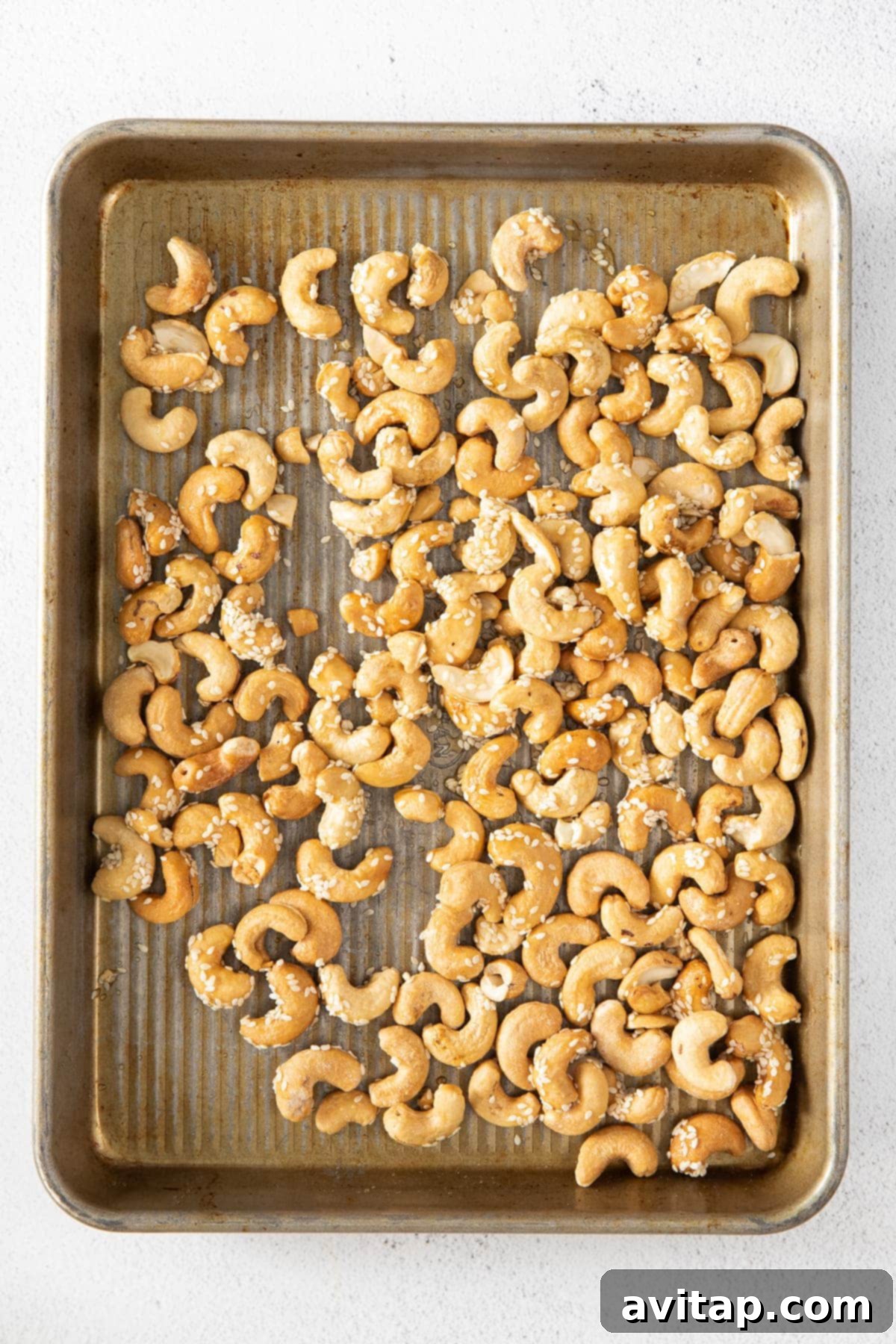 Raw cashews spread evenly on a parchment-lined baking sheet, ready for roasting.