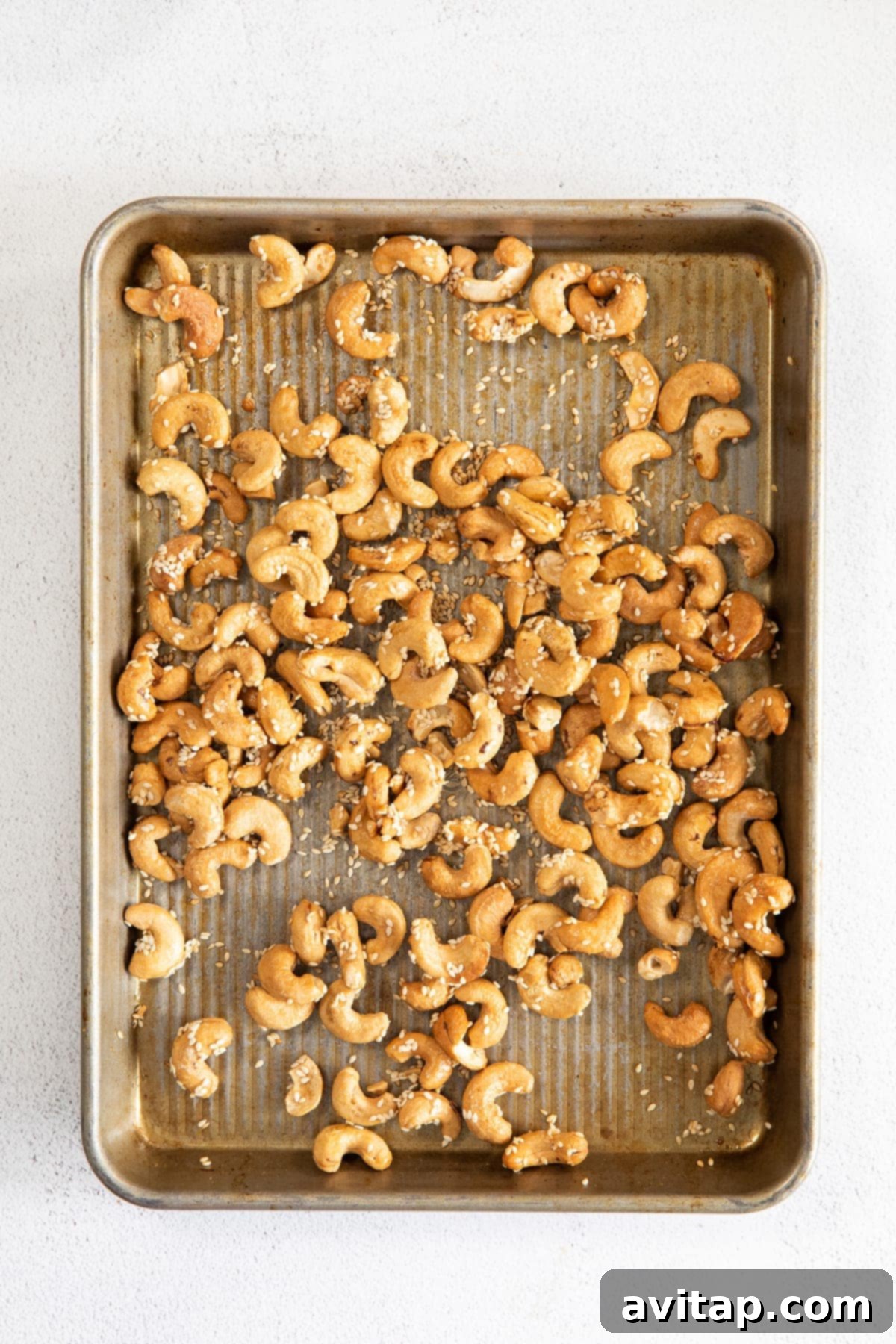 Roasted cashews glistening with maple syrup and sesame seeds, spread on a baking sheet to cool.