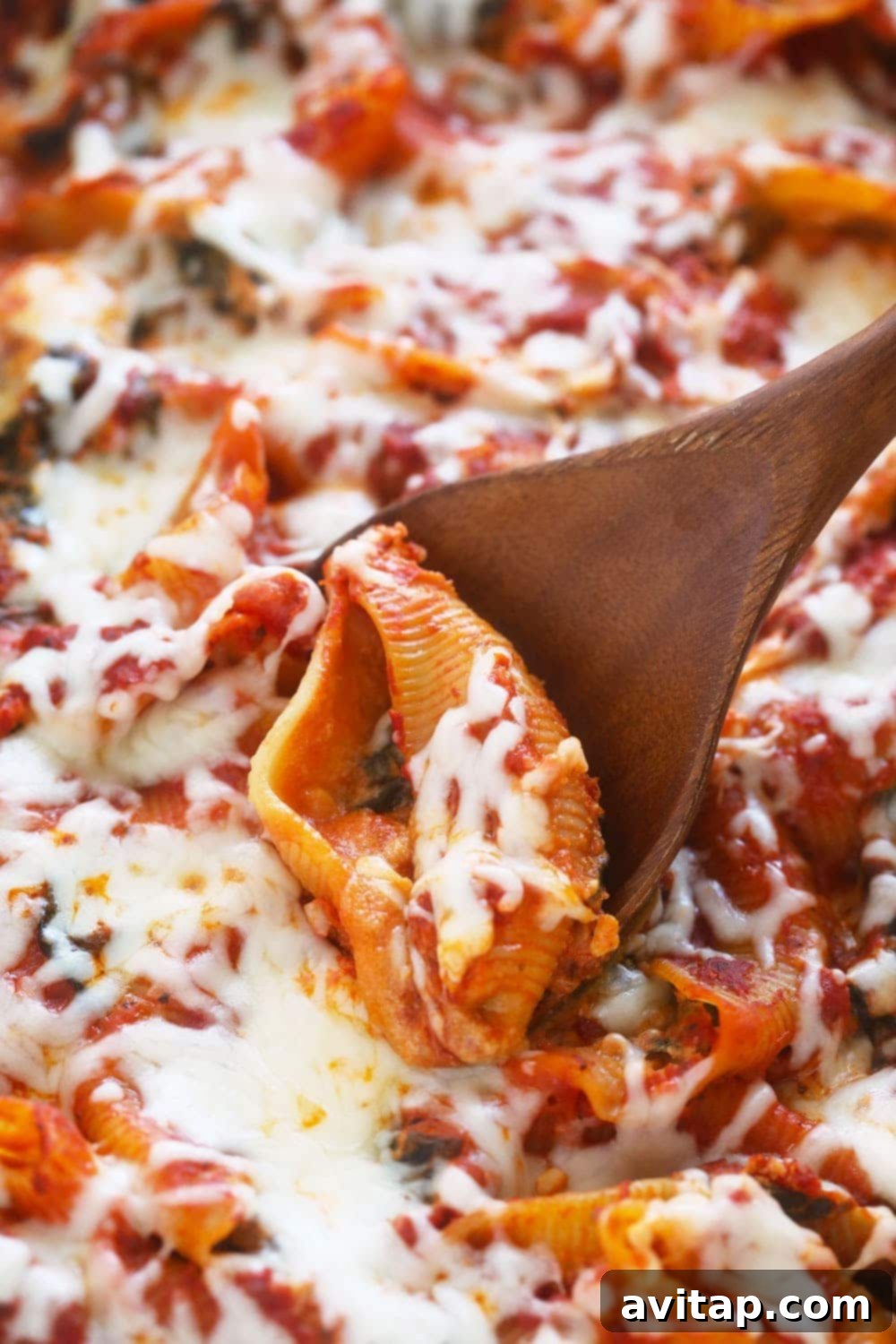 Scooping vegetarian sweet potato, spinach, and ricotta stuffed shells out of a baking dish, showcasing the creamy filling and melted cheese.