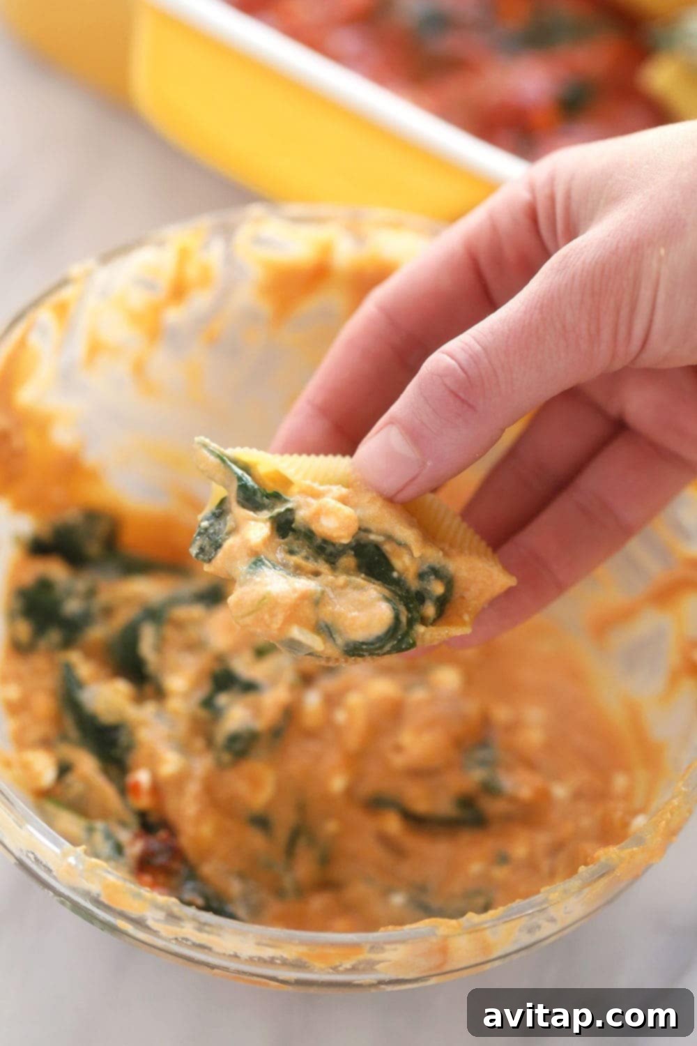 Hands carefully stuffing uncooked jumbo pasta shells with sweet potato, spinach, and ricotta filling, arranged on a cutting board.