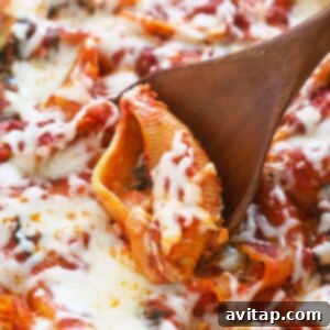 A wooden spoon is being used to scoop up a stuffed shell from a casserole dish, highlighting the rich filling.