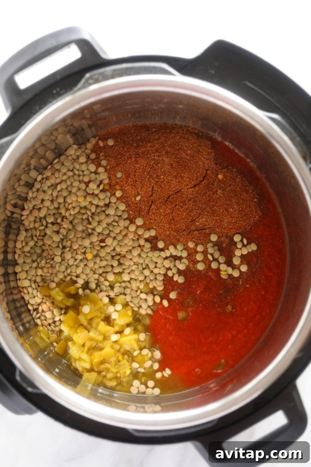 Lentils, broth, chiles, tomato sauce, and taco seasoning ready in an Instant Pot before cooking.