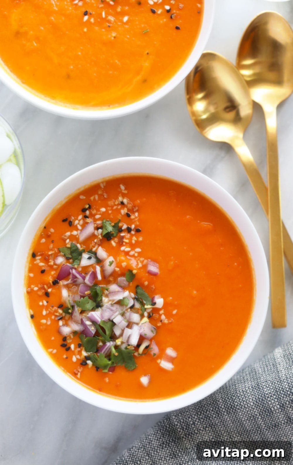 A large bowl of creamy Instant Pot Sweet Potato Carrot Ginger Soup, garnished with diced red onion and fresh cilantro.