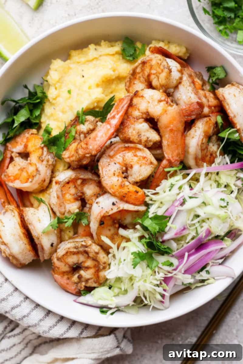 A bowl of grilled shrimp with creamy grits, garnished with chopped cilantro and served with a side of shredded cabbage and red onion.