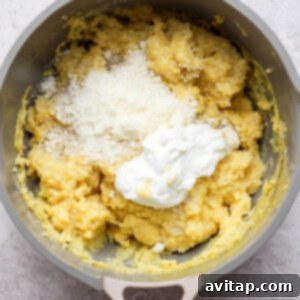 A pot containing a mixture of yellow mashed potatoes topped with grated cheese and a dollop of sour cream.