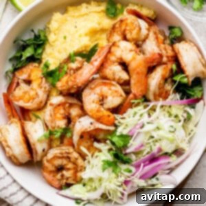 A bowl of seasoned shrimp with creamy grits, garnished with fresh cilantro, alongside a cabbage and red onion salad.