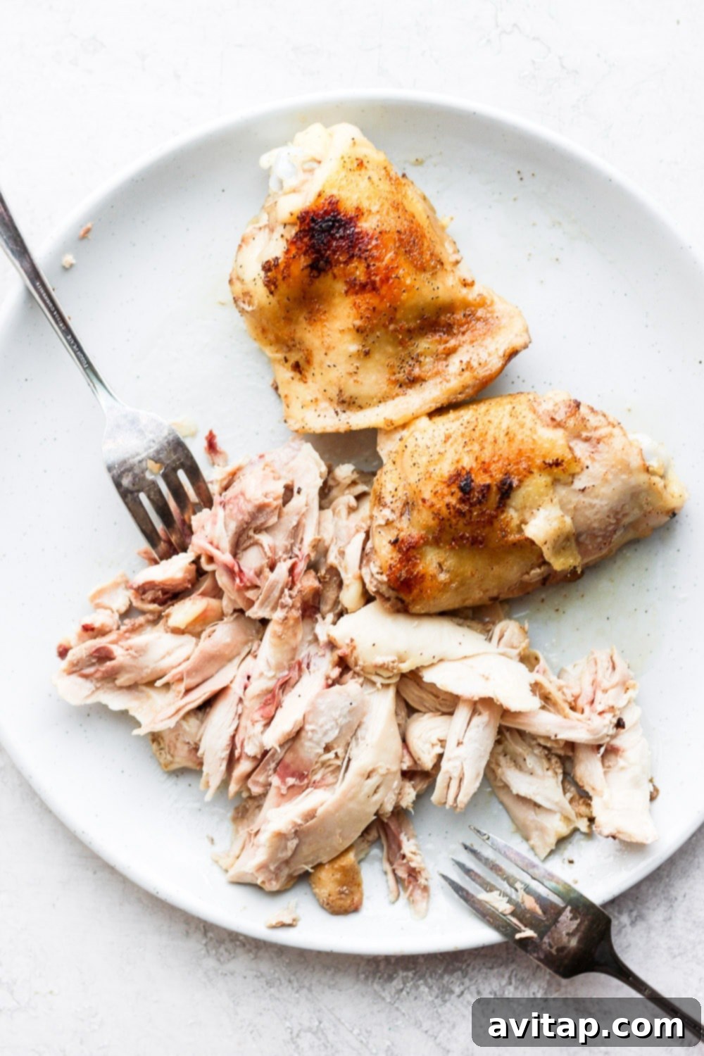 Close-up of tender chicken thighs being shredded with two forks, perfect for tacos