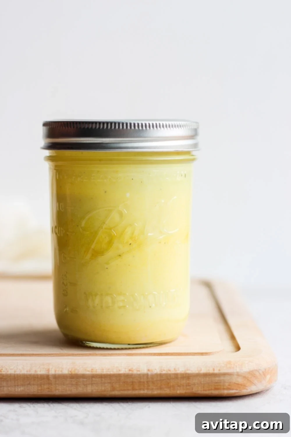 Unbelievably delicious honey mustard dressing made with a Greek yogurt base with honey and yellow mustard. Homemade honey mustard dressing in a glass jar, set on a rustic cutting board