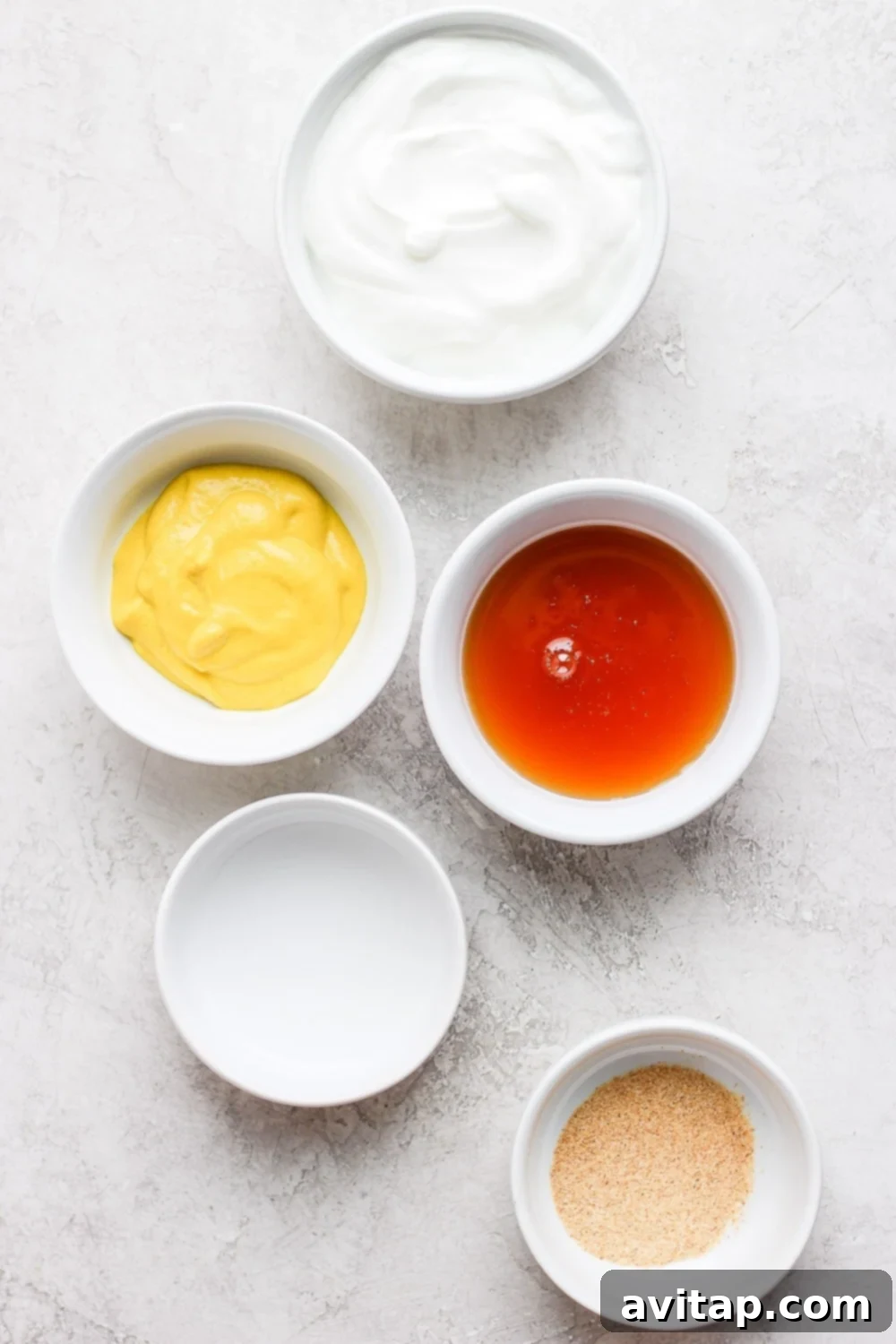 We're showing you how to make a healthy honey mustard dressing in just 5 minutes. This honey mustard dressing recipe is low fat and high protein! Bowls of honey mustard dressing ingredients laid out on a table