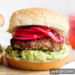 Two turkey burgers with guacamole and onions on a cutting board.