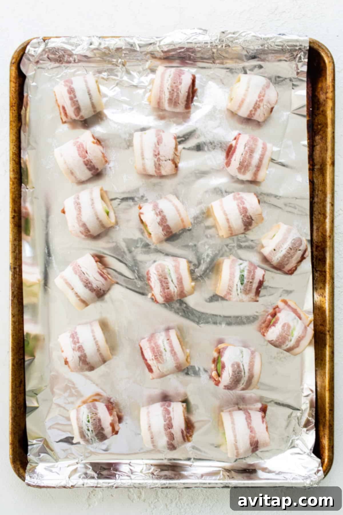 Raw bacon-wrapped Brussels sprouts arranged on a foil-lined baking sheet, ready for the oven.
