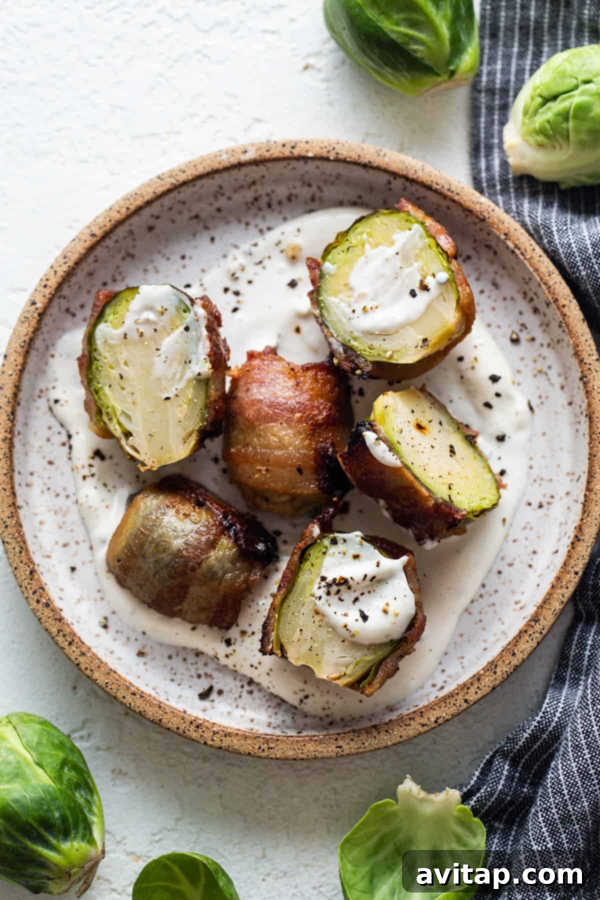 Bacon-wrapped Brussels sprouts served with a creamy dipping sauce on a plate.