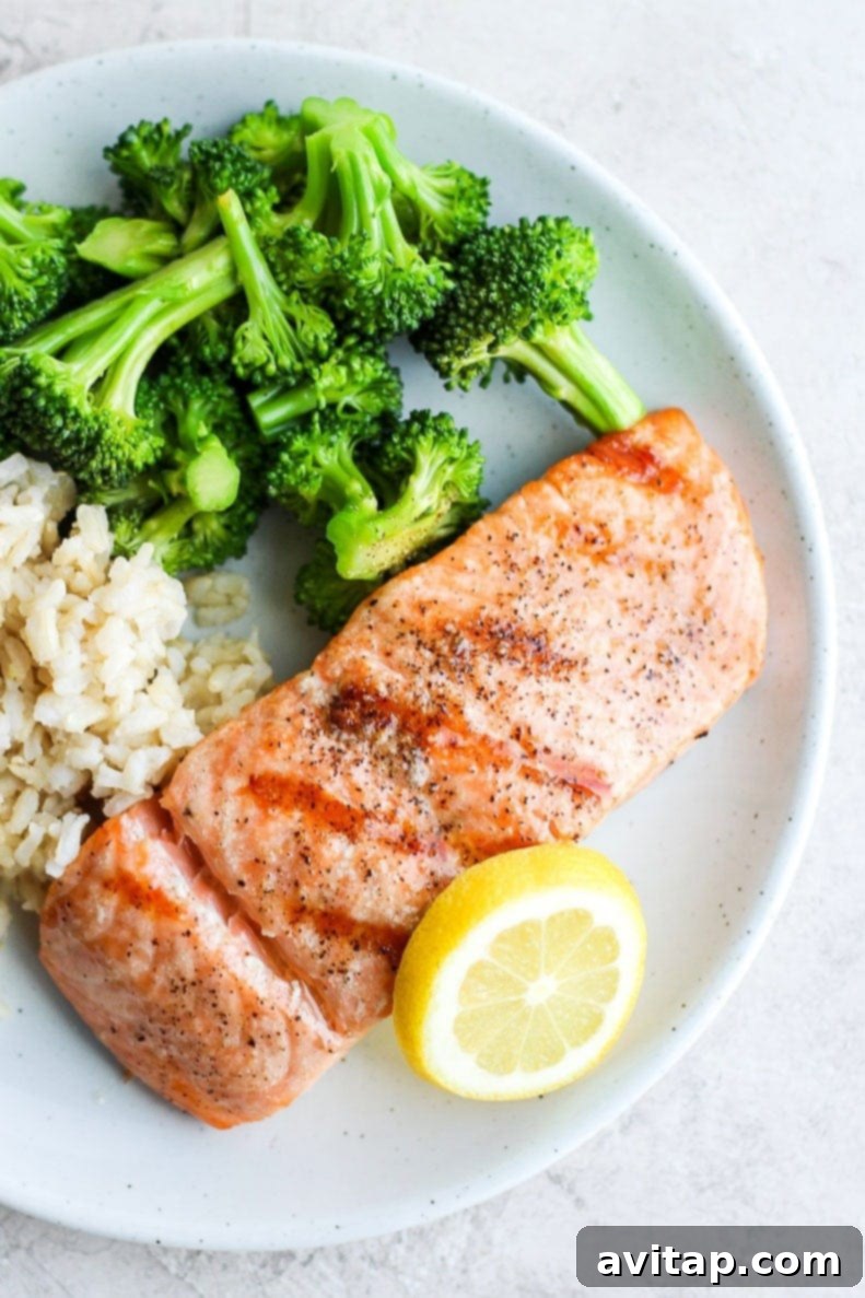 A perfectly grilled salmon fillet served on a white plate, garnished with fresh herbs, alongside vibrant green broccoli and fluffy white rice.