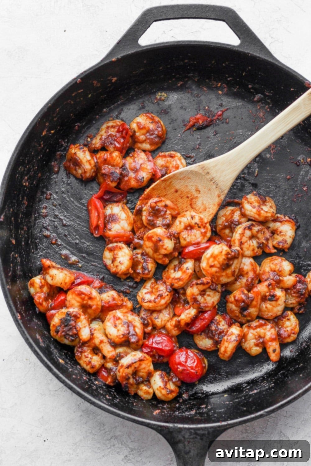 Seasoned shrimp being cooked to perfection in a hot cast iron skillet, alongside cherry tomatoes