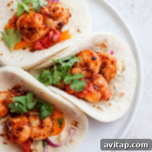 Three shrimp tacos on a white plate, garnished with fresh cilantro.